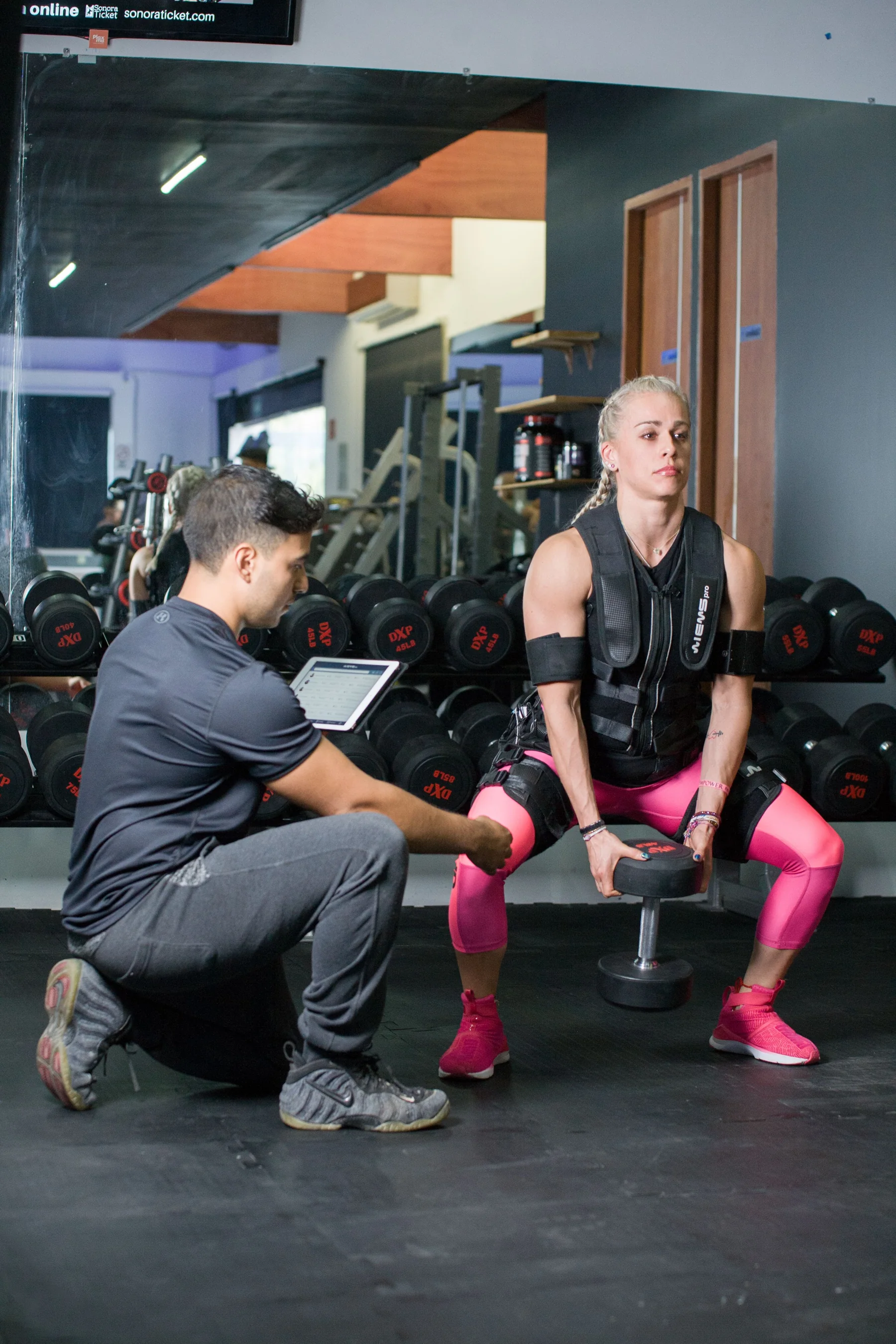 A personal trainer supporting a woman during a weighted exercise.