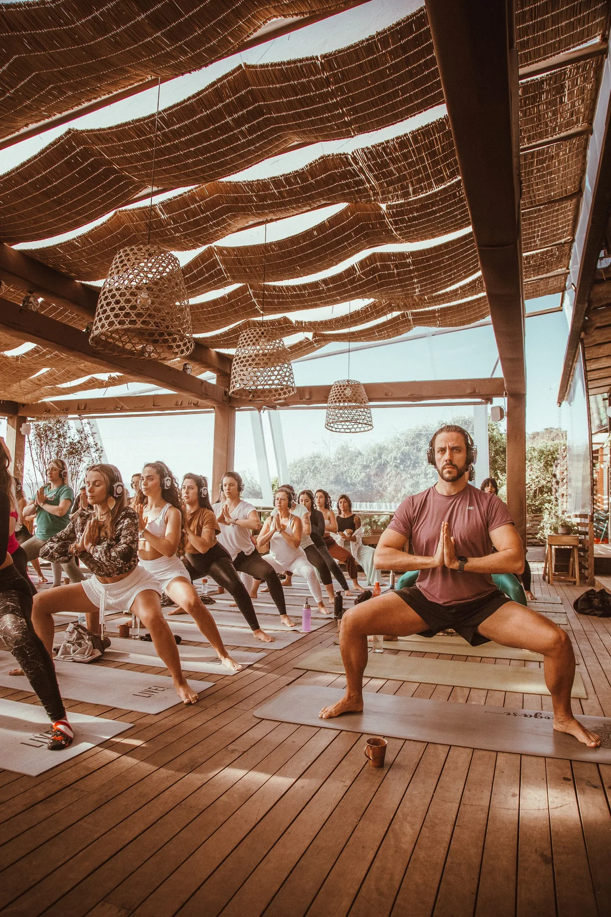 A group practising yoga beneath a woven canopy on a wooden terrace.