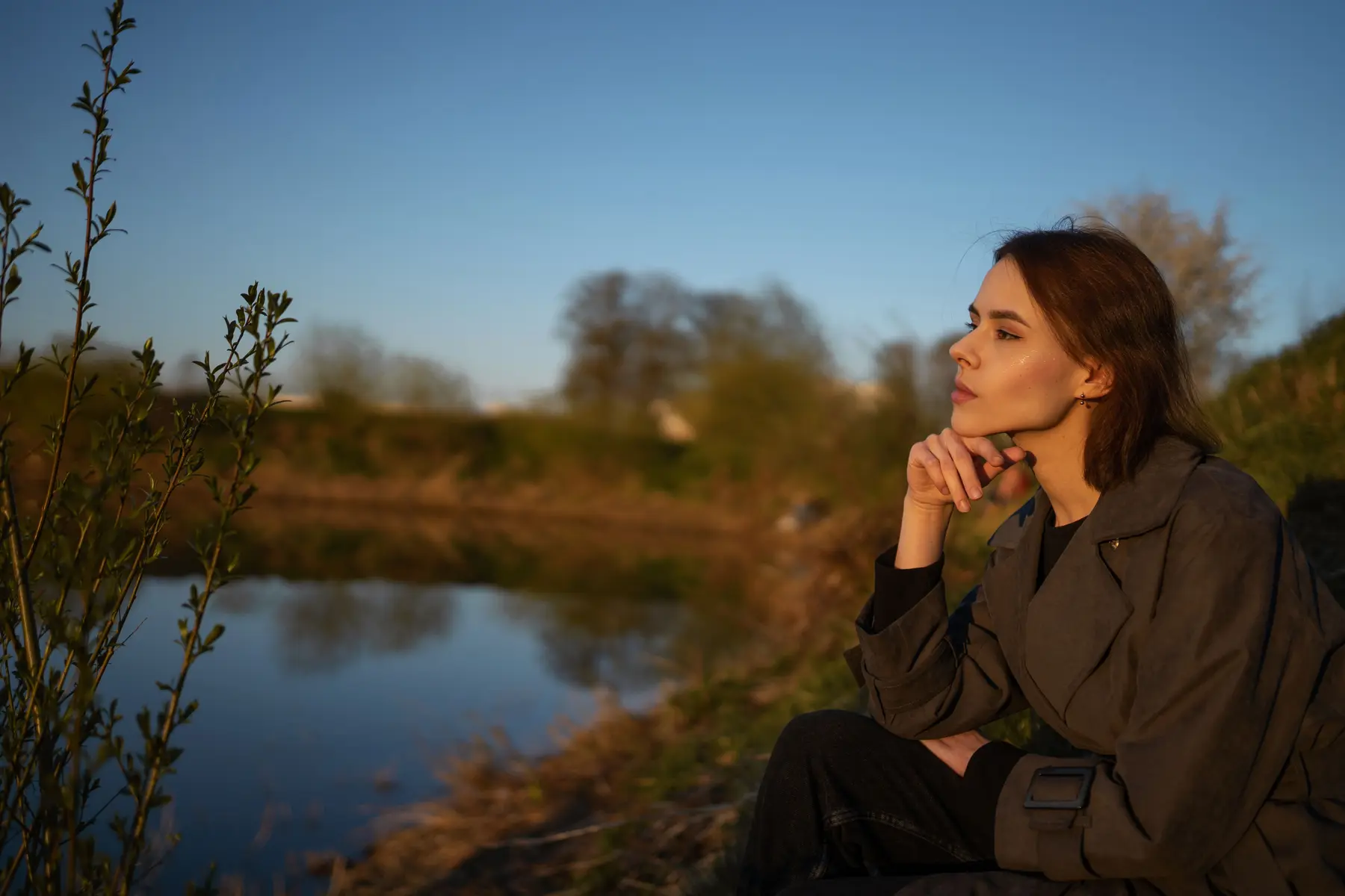 A woman sitting thoughtfully beside a lake.